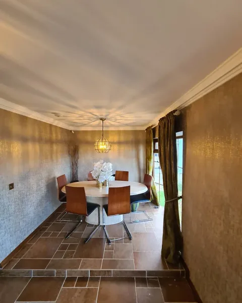 Dining room with textured gold walls, white cornicing and a round dining table