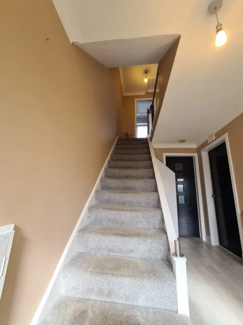 Staircase with warm neutral walls, white trim and grey carpet